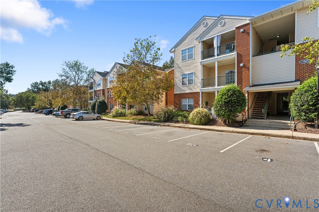 Multi-story residential building featuring brick and vinyl siding, private covered balconies with metal railings, and dedicated surface parking