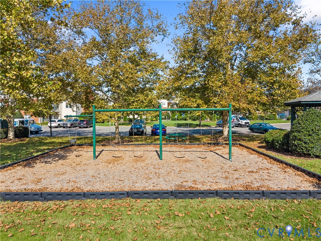 Outdoor recreation area featuring a metal swing set, wood-chip surface, and mature perimeter trees