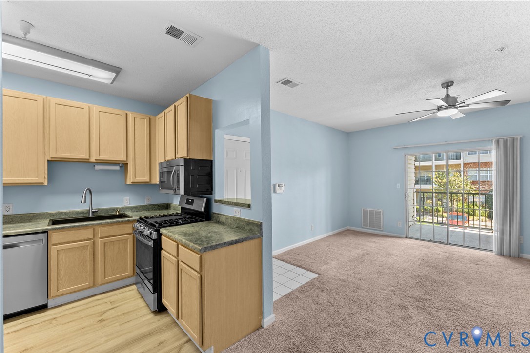 Kitchen featuring light-finish cabinetry, stone-texture countertops, a stainless steel gas range, and a dishwasher, with sliding glass doors opening to a balcony