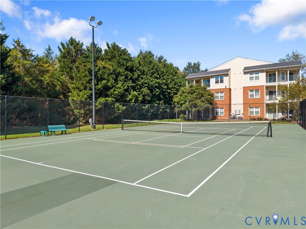 Hard-surfaced tennis court featuring perimeter fencing and overhead area lighting