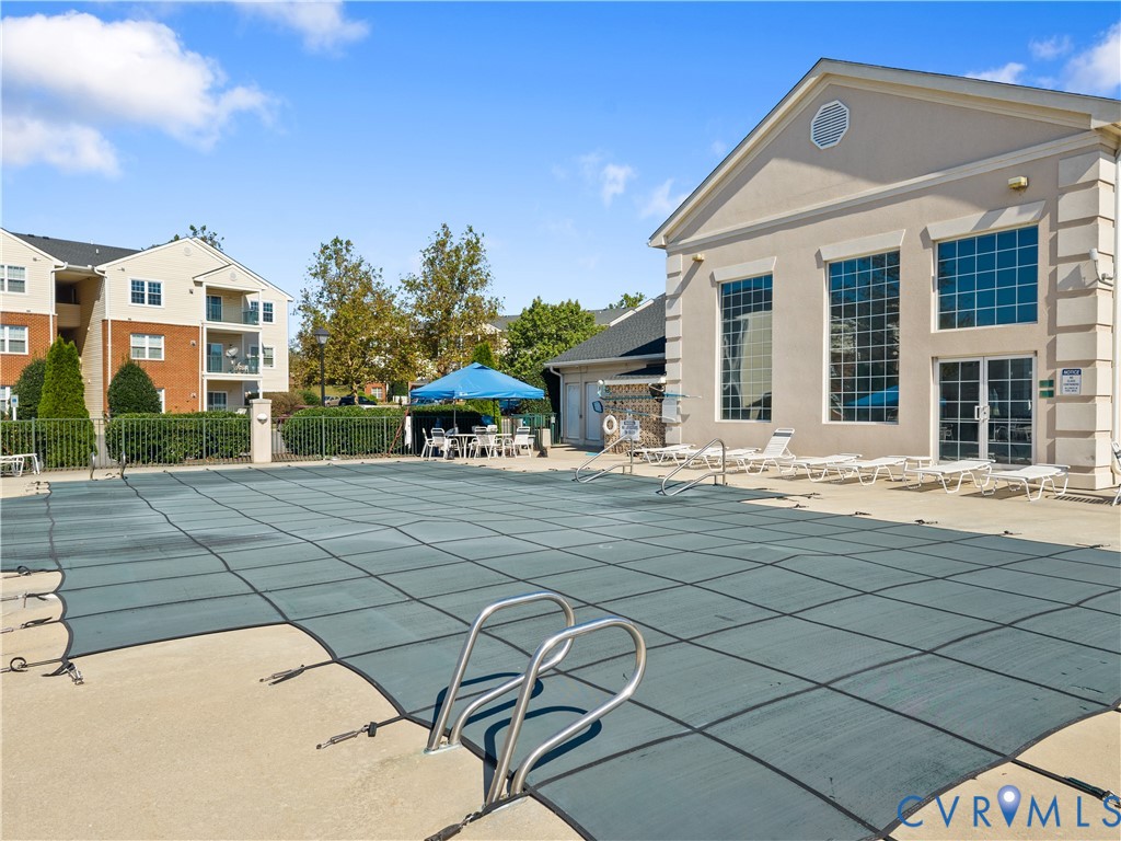 Swimming pool with a fitted safety cover, concrete decking, and multi-story clubhouse featuring large-pane windows and a pediment roofline