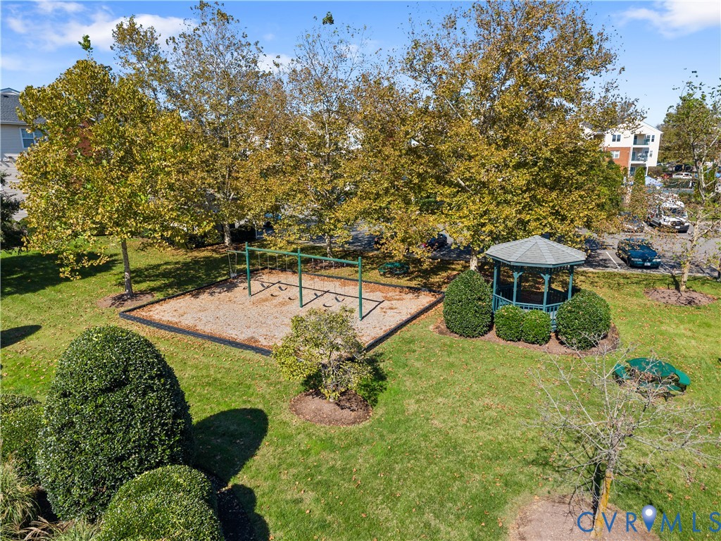 Common area grounds featuring a gazebo, swing set, manicured lawn, and mature trees