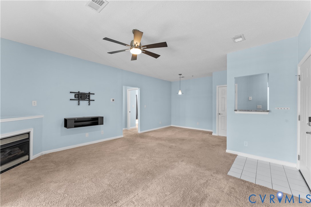 Gas fireplace with a stone surround, neutral carpeting, ceiling fan with integrated lighting, tiled entryway, and wall-mounted cabinetry