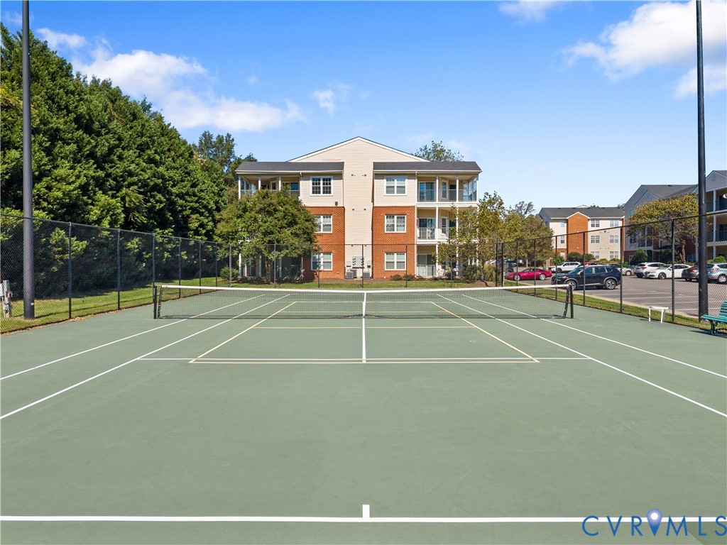 Tennis court featuring a paved surface, perimeter chain-link fencing, and stadium-style lighting poles