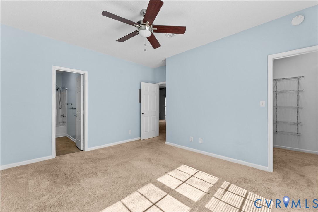 Spacious room featuring neutral carpeting, a ceiling fan with dark wood-finish blades, and built-in metal shelving within the storage area