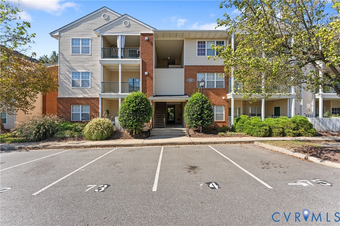 Multi-story building exterior featuring vinyl siding, brick masonry, private balconies, and assigned asphalt parking