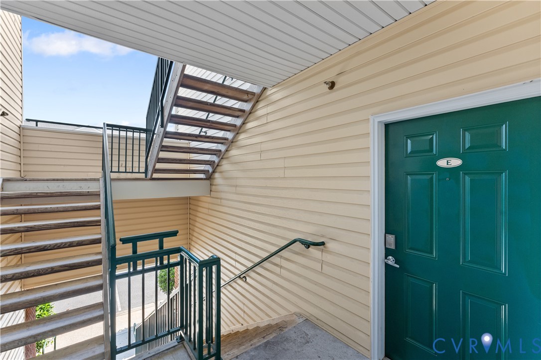 Exterior entryway featuring horizontal siding, a solid panel door with metallic hardware, and an open-air metal staircase with railing