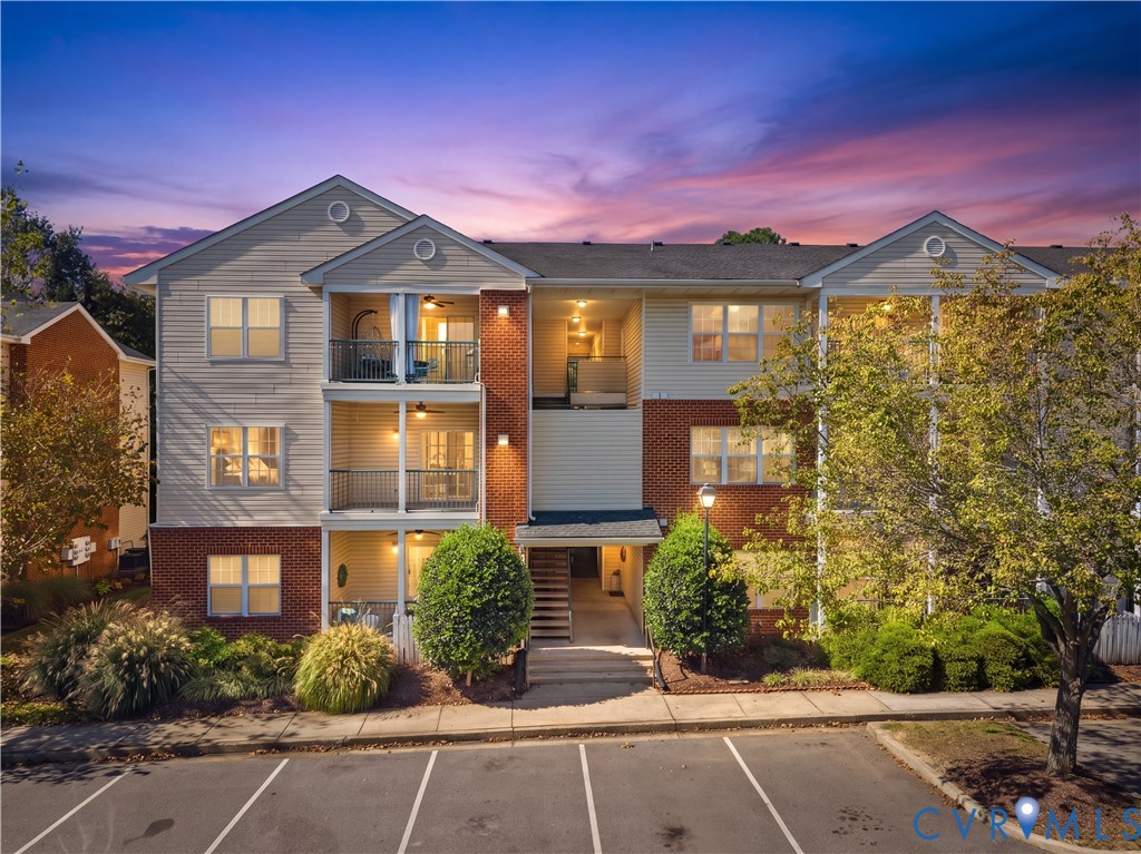 Multi-story residential building featuring brick and horizontal siding exterior, private covered balconies, and paved surface parking