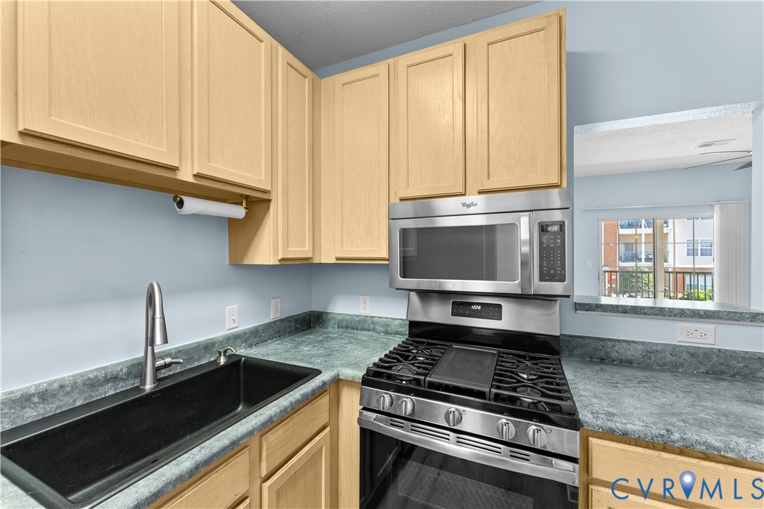 Kitchen featuring light-finish cabinetry, a black undermount sink with a high-arc faucet, solid-surface countertops, and stainless steel appliances including a gas range and over-the-range microwave