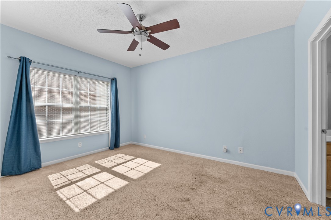 Neutral-toned carpeting, five-blade ceiling fan with integrated lighting, and multi-pane window