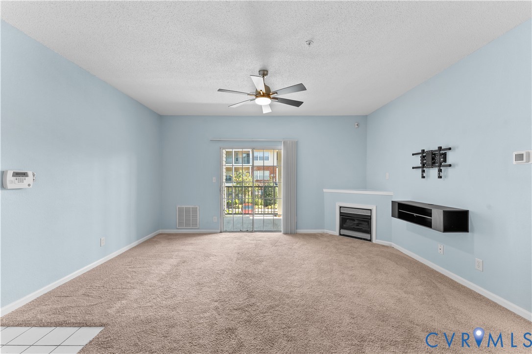 Living area featuring wall-to-wall carpeting, ceiling fan, sliding glass door, fireplace with mantel, and wall-mounted shelving