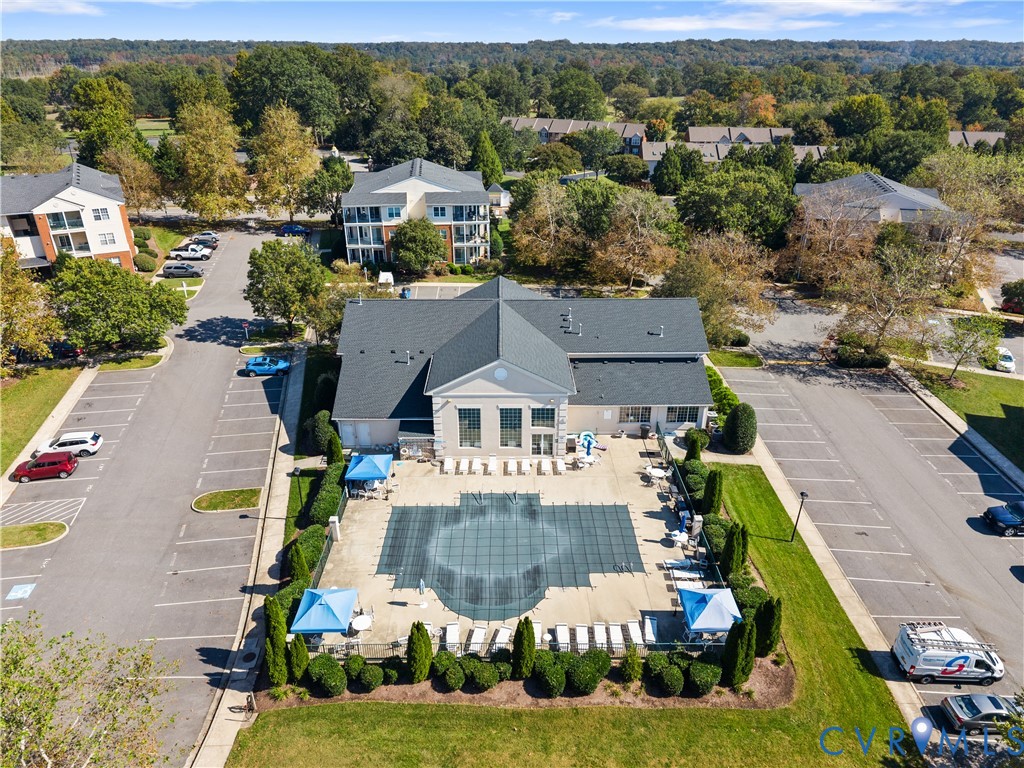 Community clubhouse featuring a shingled roof, exterior patio, and gated swimming pool with surrounding landscaping and dedicated parking