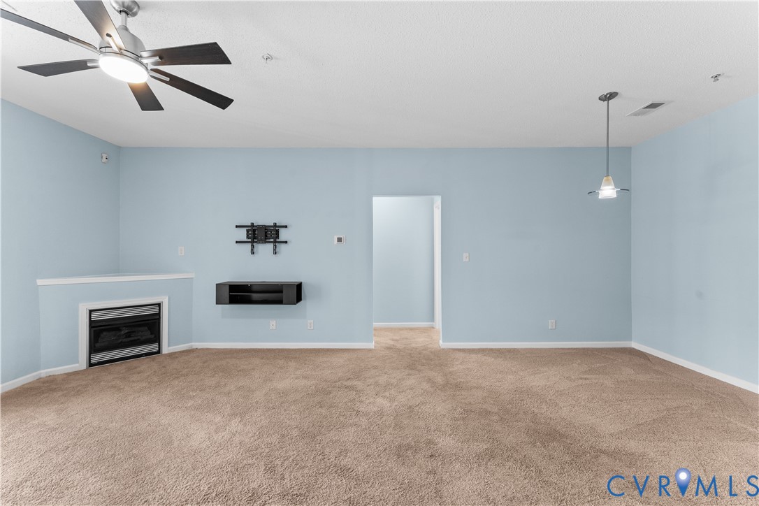 Interior space featuring a corner fireplace with a mantel, wall-mounted console, ceiling fan with light fixture, pendant lighting, and neutral carpeting