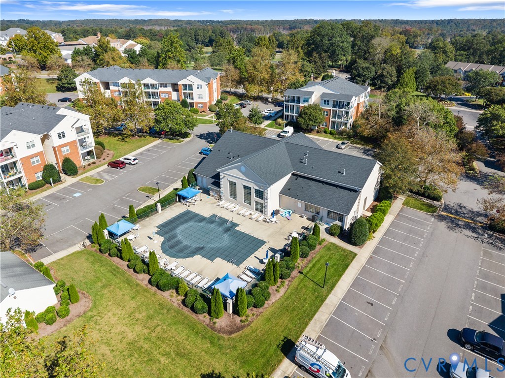 Community swimming pool with a concrete deck, manicured shrubbery, and paved parking area