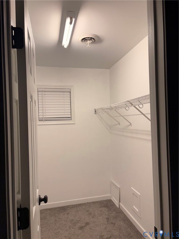 White interior walls, gray carpet flooring, window with blinds, wire shelving, and overhead fluorescent lighting