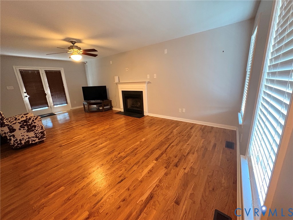 Hardwood flooring, fireplace with mantel, ceiling fan, double French doors, and window blinds Hardwood flooring, fireplace with mantel, ceiling fan, double French doors, and window blinds