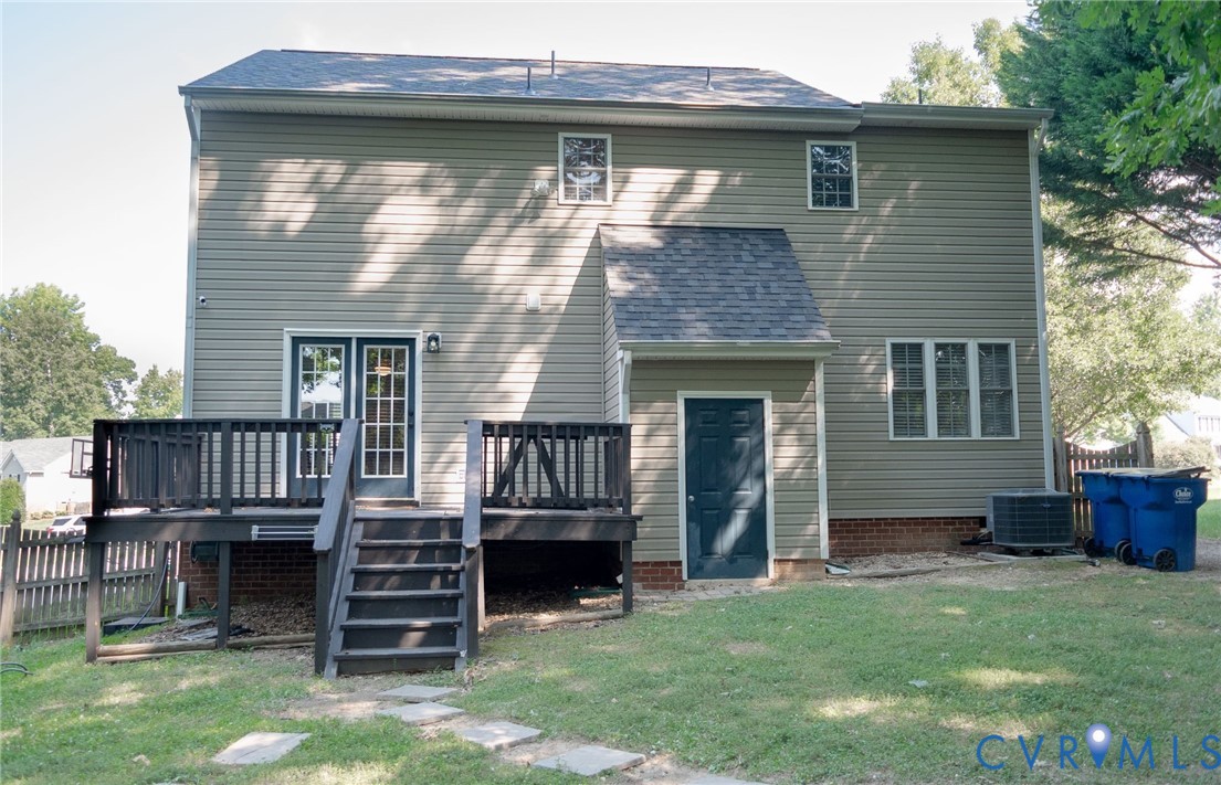 Rear exterior with a black wood deck, sliding glass doors, and a ground-level door Rear exterior with a black wood deck, sliding glass doors, and a ground-level door
