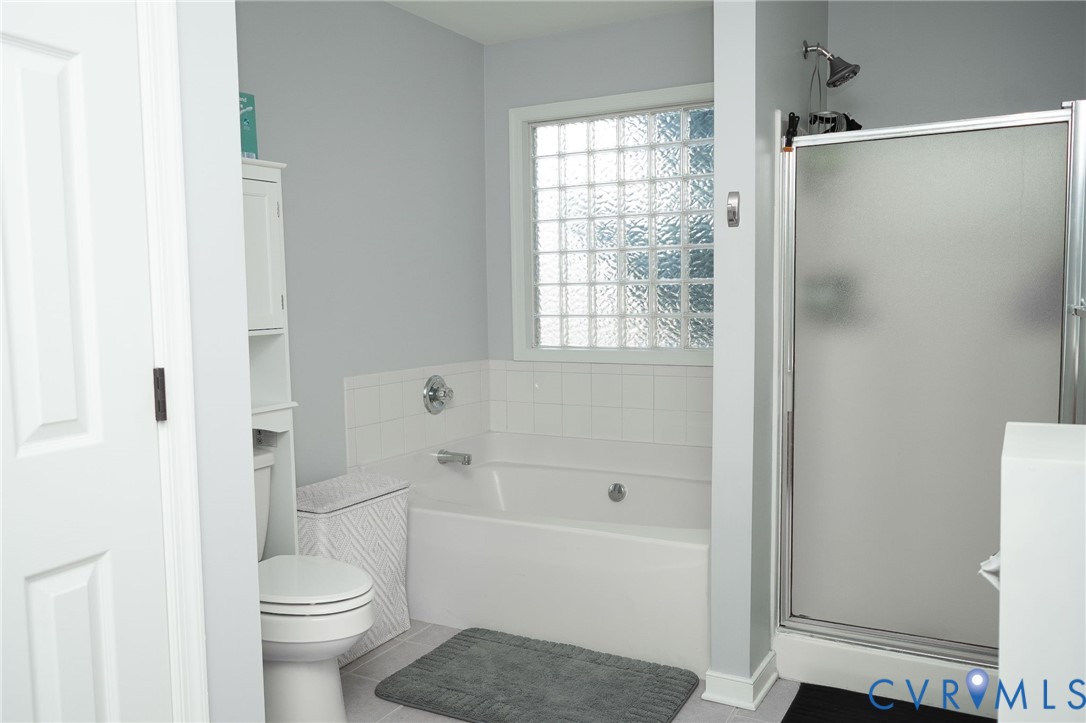 Bathtub with white tile surround, glass block window, and adjacent shower with frosted glass enclosure