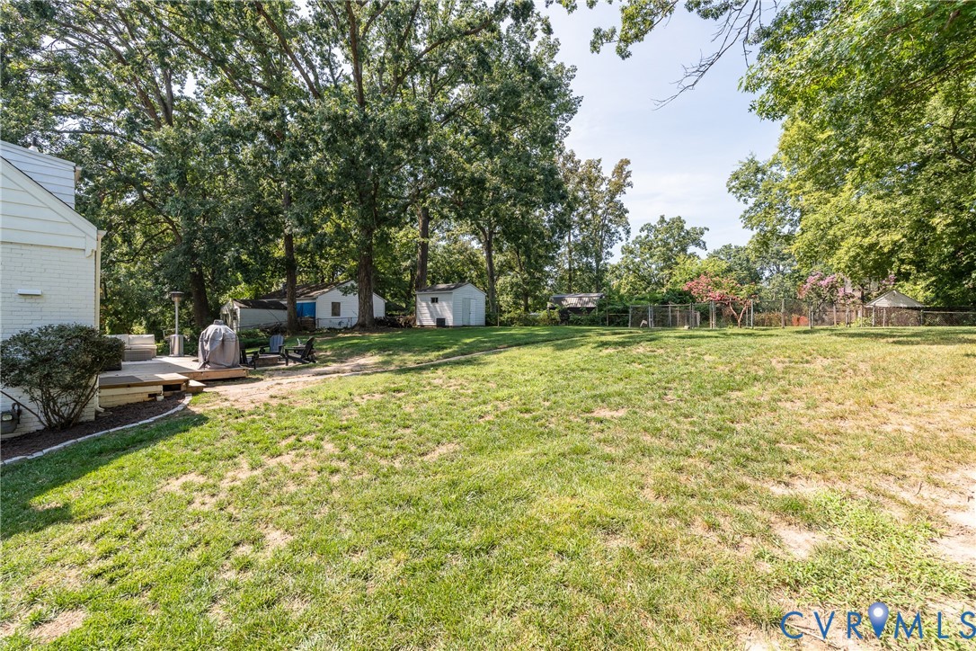 Expansive grassy lawn with mature trees, featuring a raised deck, and two detached storage sheds