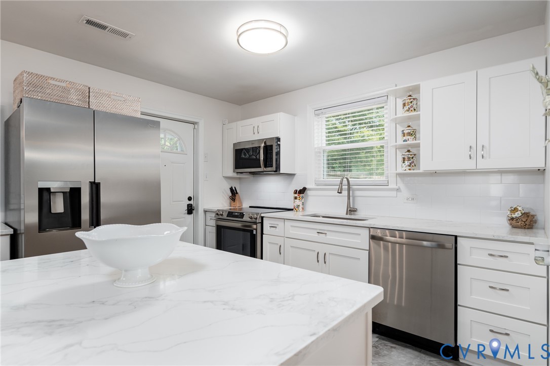 White shaker-style cabinetry, stainless steel appliances, white subway tile backsplash, and light-toned countertops