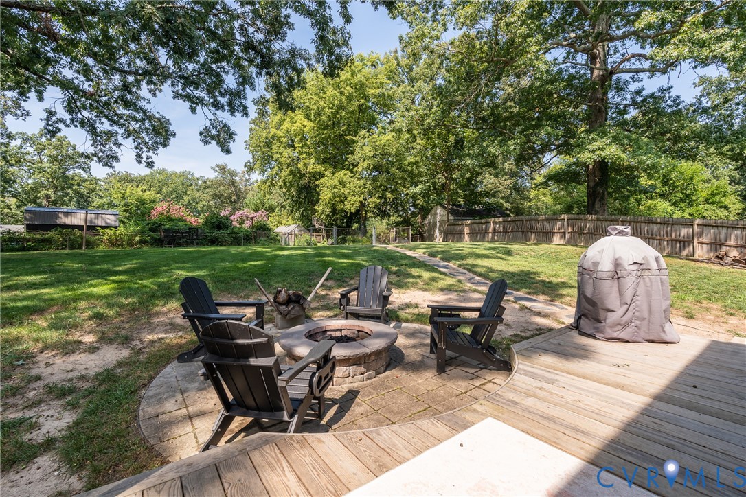 Expansive backyard featuring a wood deck, a stone fire pit with paver surround, and a fenced perimeter