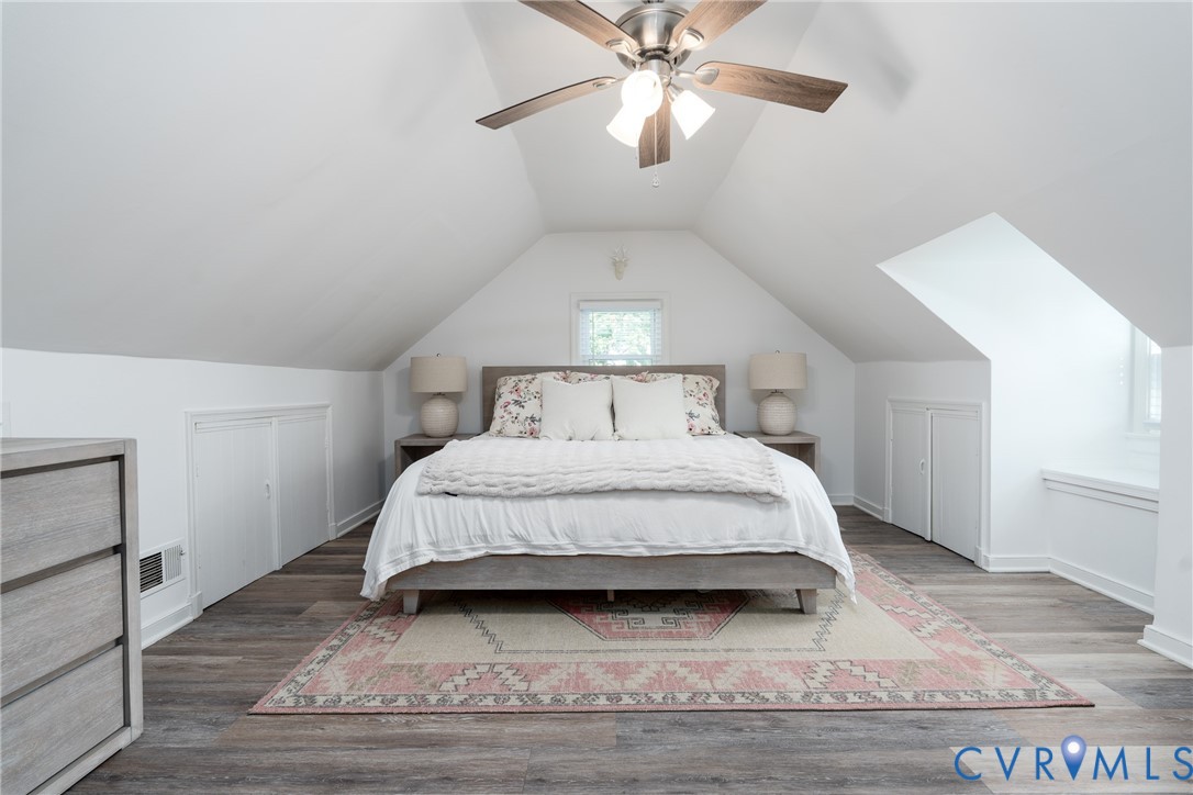 Vaulted ceiling with a ceiling fan, wood-finish flooring, two built-in closet doors, and a window