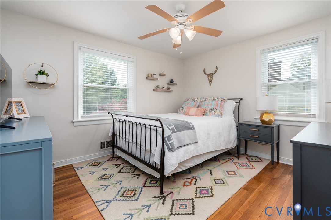 Bright bedroom offering hardwood flooring, a ceiling fan with integrated lighting, and ample natural light from multiple windows