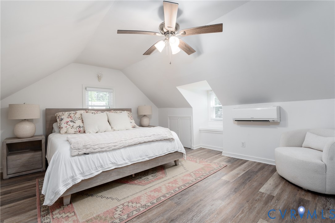Attic room featuring a sloped ceiling, wood-finish flooring, a ceiling fan with integrated lighting, and a wall-mounted air conditioning unit