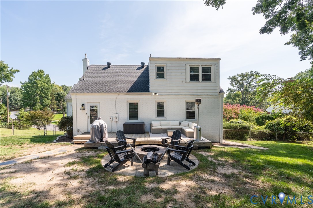 Expansive backyard with a wooden deck, stone fire pit, and mature trees