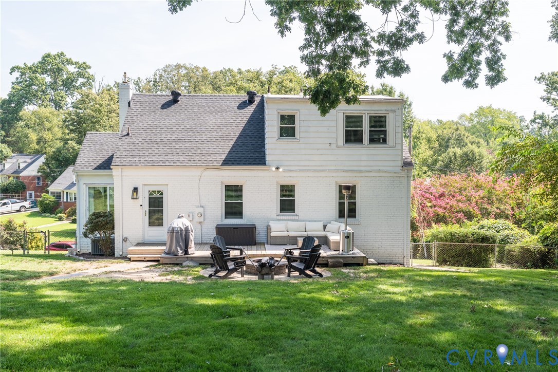 Expansive rear yard with a manicured lawn, an outdoor deck, and a fire pit area
