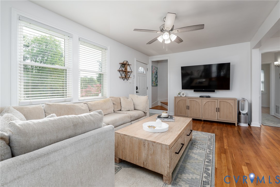 Hardwood flooring, white walls, multiple windows, ceiling fan, and a built-in media console
