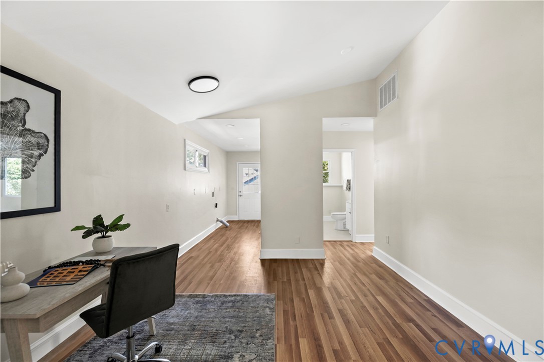 Vaulted ceiling with a flush-mount light fixture, wood-finish flooring, and white trim
