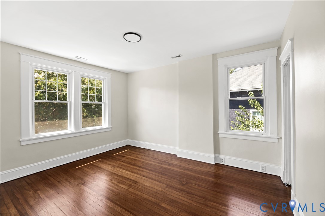 Hardwood flooring, painted walls, white trim, multiple windows with grid panes, and a flush-mount ceiling light