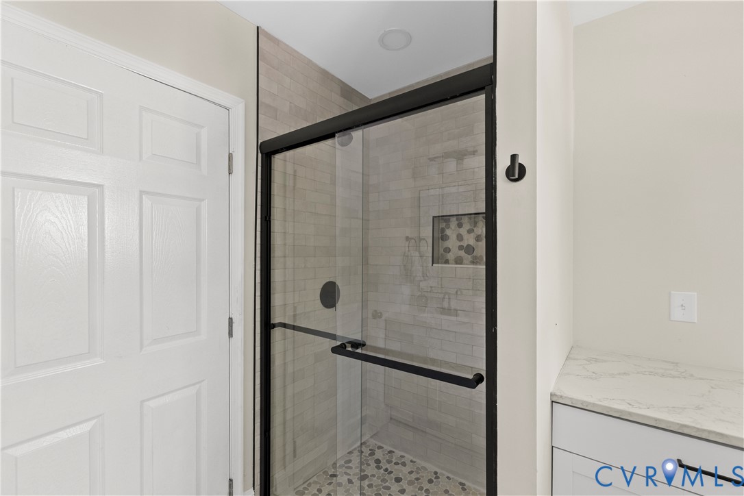 Glass-enclosed shower with a matte black frame, tiled walls, and a pebble-style floor