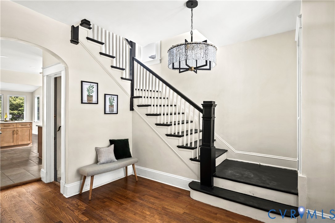 Hardwood flooring, painted staircase with white risers and black treads, black newel post and handrail, and an arched doorway Hardwood flooring, painted staircase with white risers and black treads, black newel post and handrail, and an arched doorway