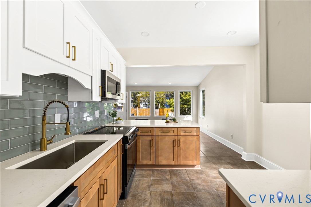 Modern kitchen featuring white upper cabinetry, natural wood-finish lower cabinetry, light-toned countertops, a subway tile backsplash, and stainless steel appliances Modern kitchen featuring white upper cabinetry, natural wood-finish lower cabinetry, light-toned countertops, a subway tile backsplash, and stainless steel appliances
