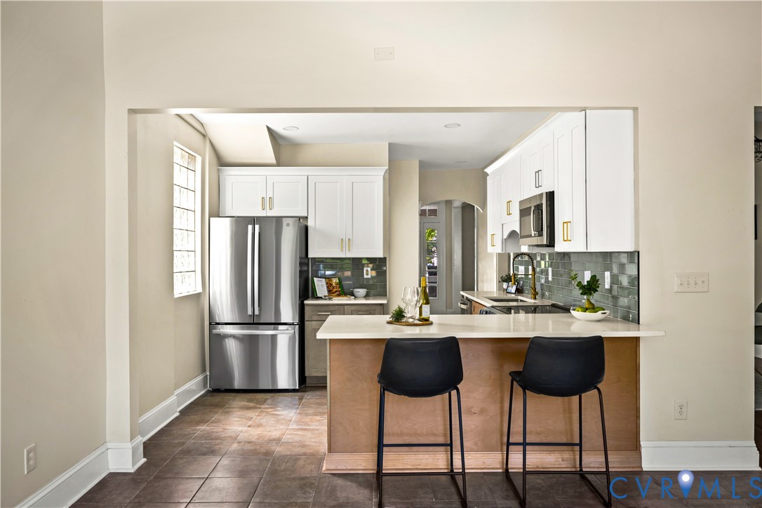 Stainless steel refrigerator, white cabinetry, dark subway tile backsplash, light countertop, and a built-in microwave Stainless steel refrigerator, white cabinetry, dark subway tile backsplash, light countertop, and a built-in microwave