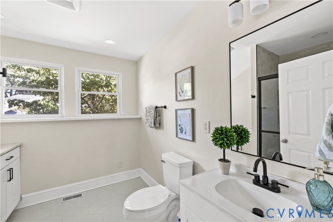 Bathroom featuring hexagonal floor tiling, a white vanity with integrated sink, black-finish faucet, and two casement windows