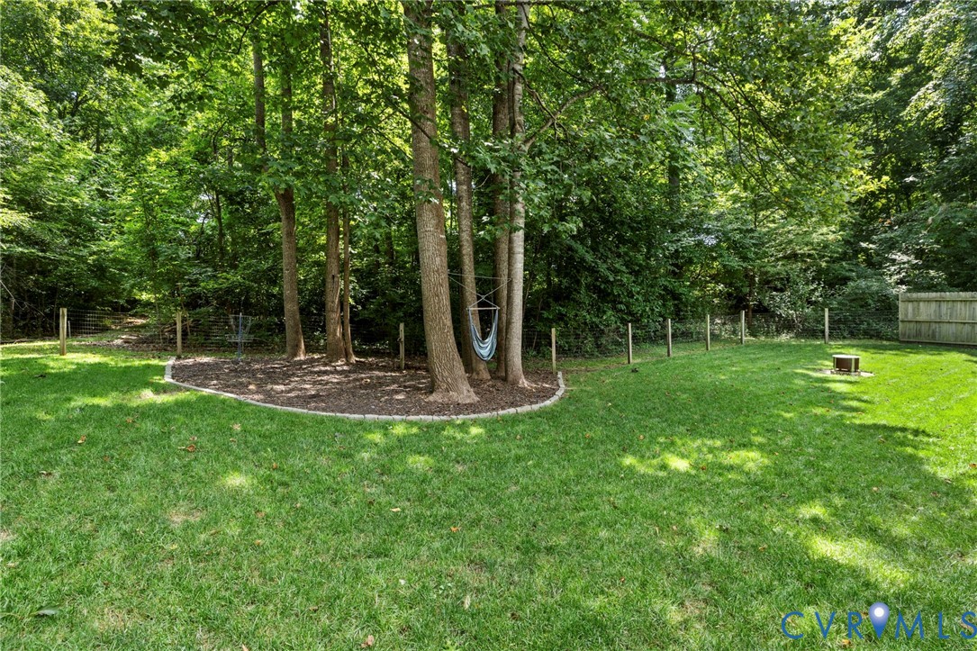 Expansive grassy yard with mature trees, a defined mulch bed, and a wooden privacy fence
