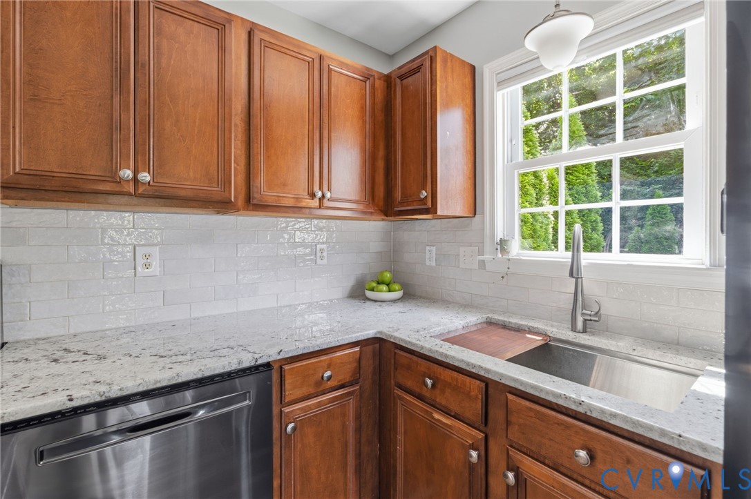 Wood-finish cabinetry paired with white subway tile backsplash, light-toned countertops, stainless steel sink with a pull-down faucet, and a large window