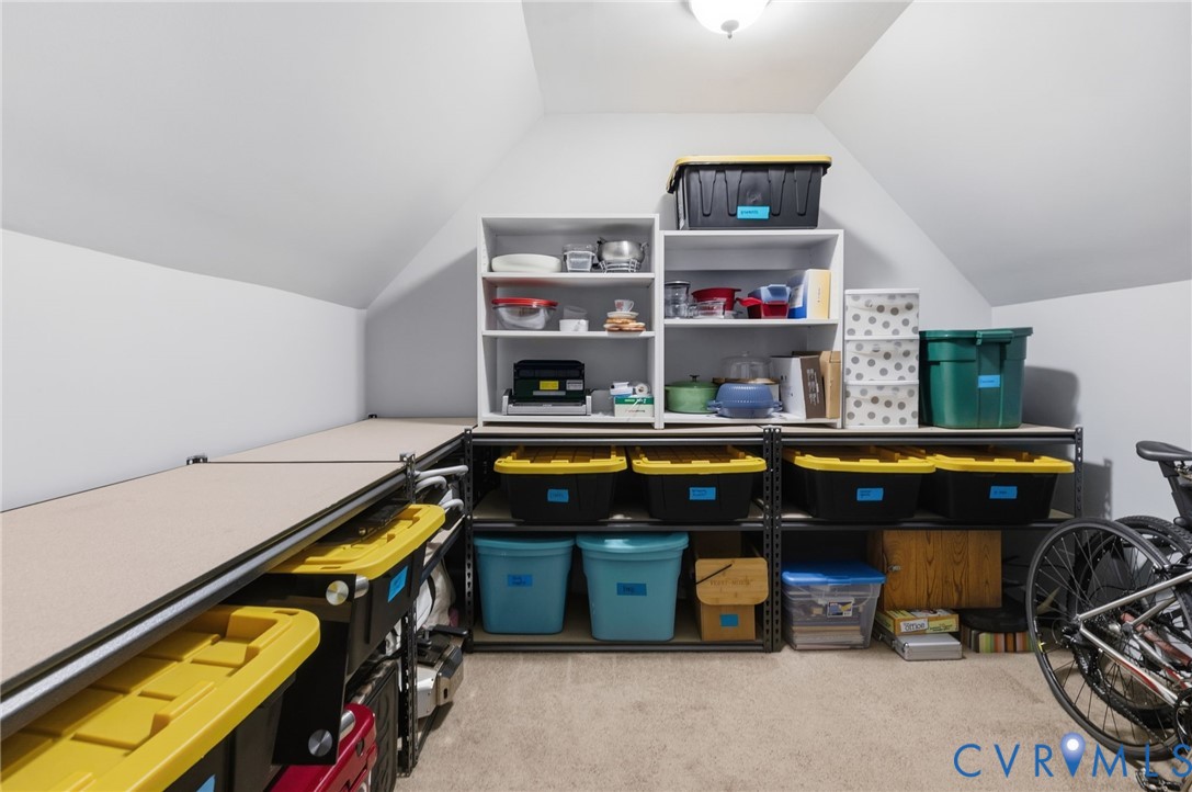 Attic storage area featuring sloped ceilings, built-in shelving, and carpeted flooring
