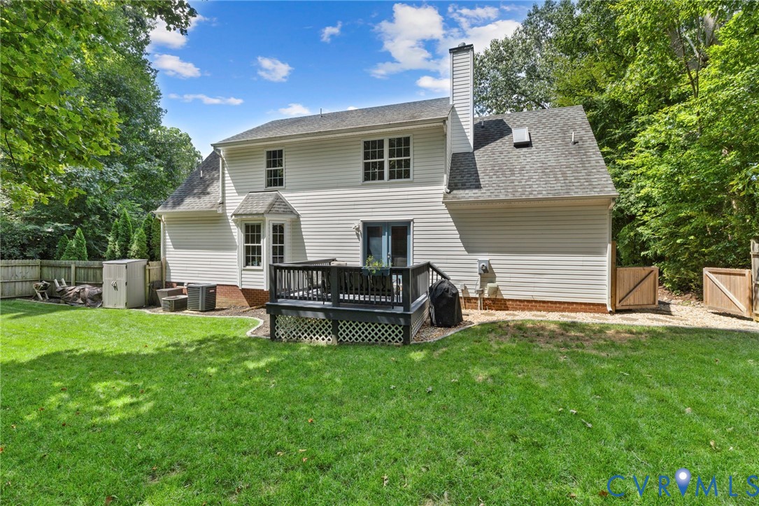 Expansive grassy yard with a multi-level deck, white siding exterior, and bay window