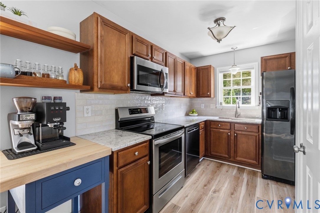 Kitchen featuring wood-finish flooring, wood cabinetry, stone countertops, a subway tile backsplash, and stainless steel appliances