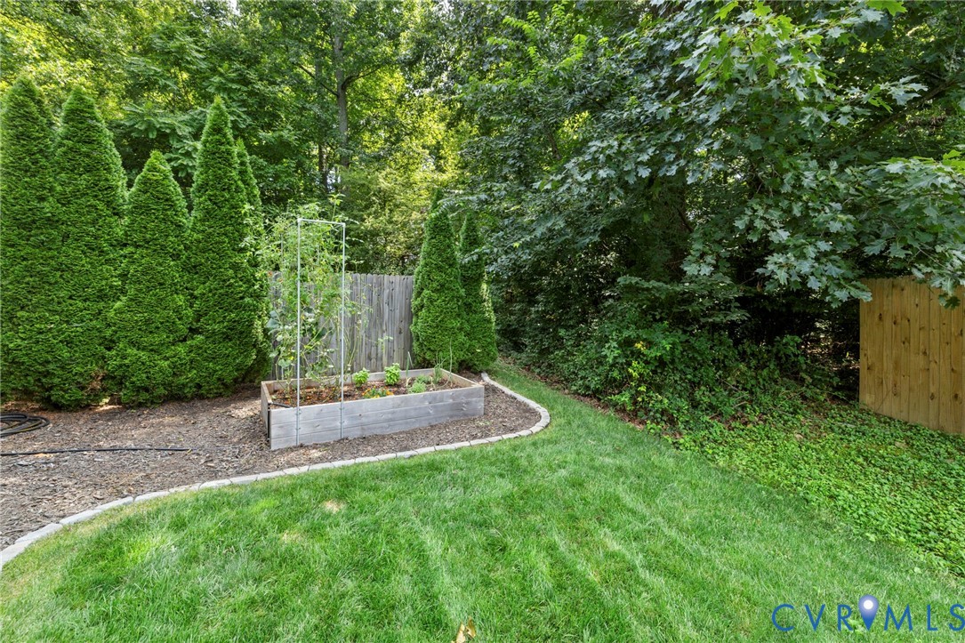 Curved lawn area with a raised planter bed, mature evergreen shrubs, and wood privacy fencing