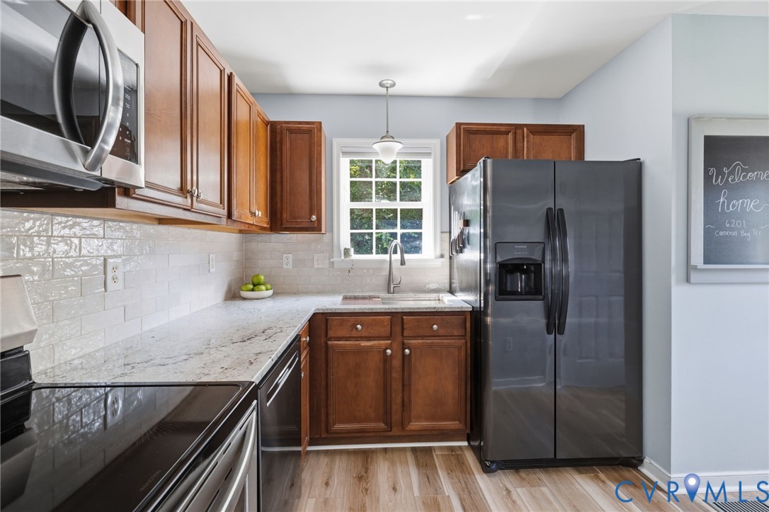 Wood-finish flooring, L-shaped countertop, white subway tile backsplash, stainless steel appliances, and wood cabinetry