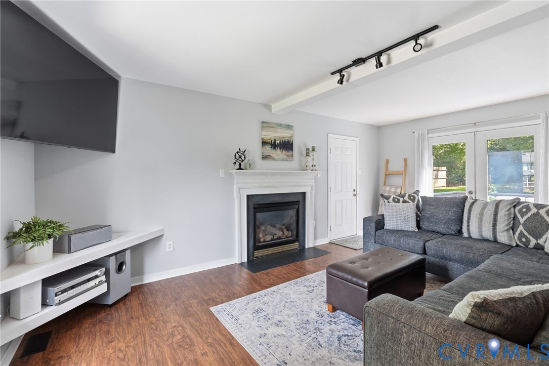 Living area featuring wood-finish flooring, a white mantel fireplace with a black hearth, track lighting, and double glass panel doors