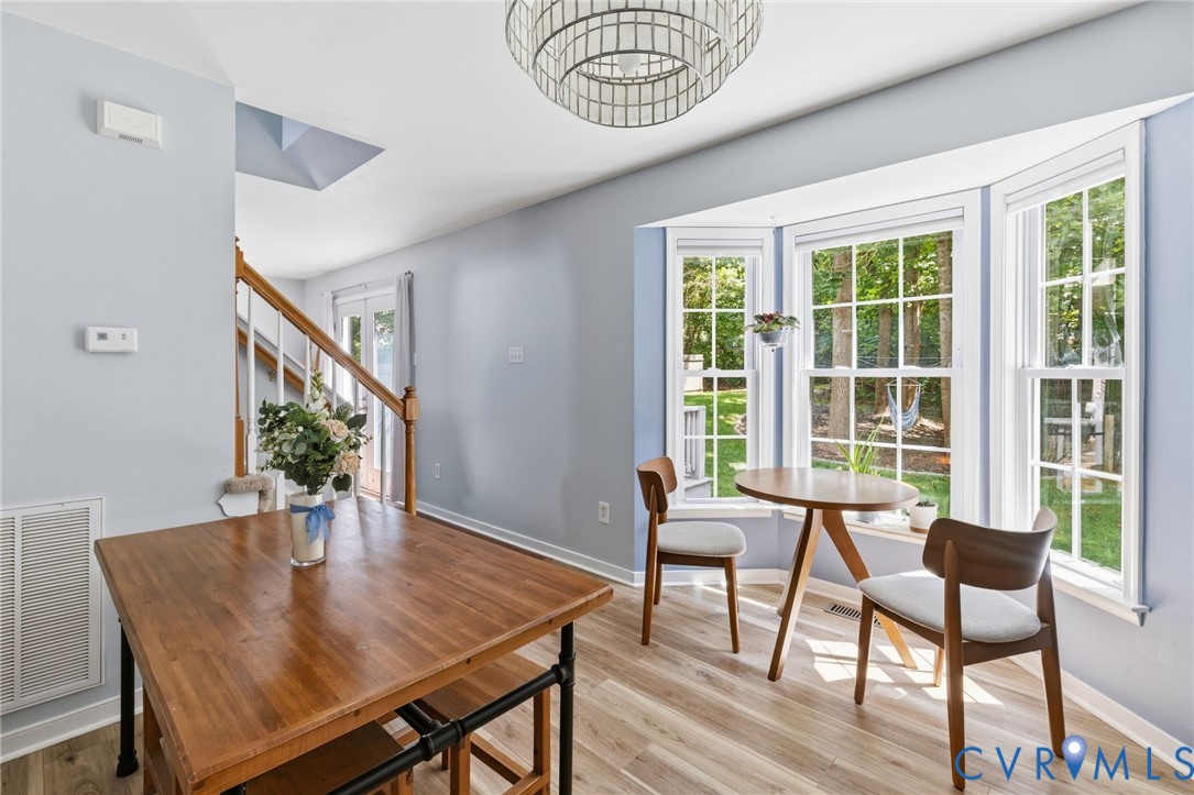 Bay window with multiple panes, wood-finish flooring, staircase with wood handrail, light blue wall paint, and a decorative ceiling light fixture