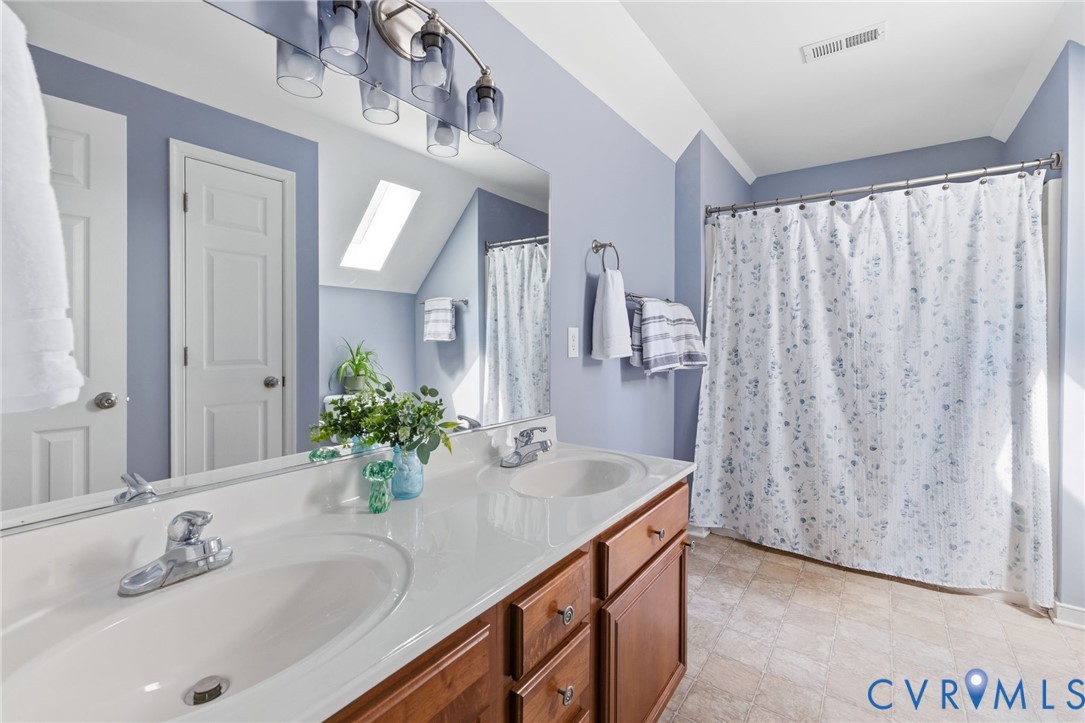 Dual vanity with undermount sinks, brown wood-finish cabinetry, and a skylight