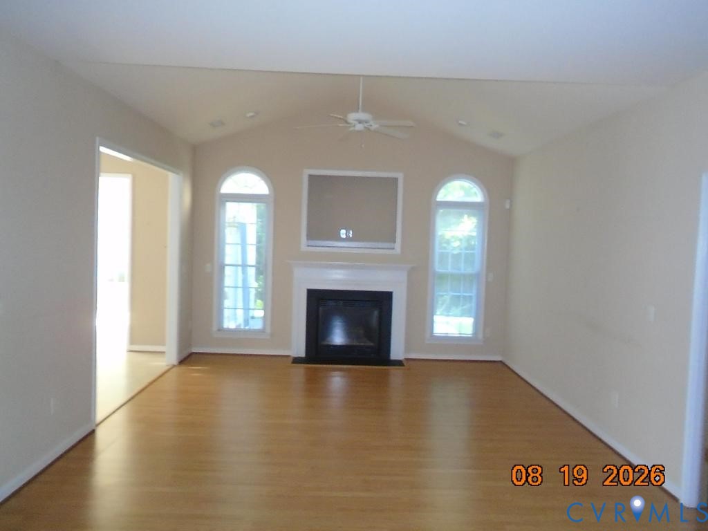 Spacious living area featuring vaulted ceilings, wood-finish flooring, a fireplace with a white mantel, and arched windows Spacious living area featuring vaulted ceilings, wood-finish flooring, a fireplace with a white mantel, and arched windows