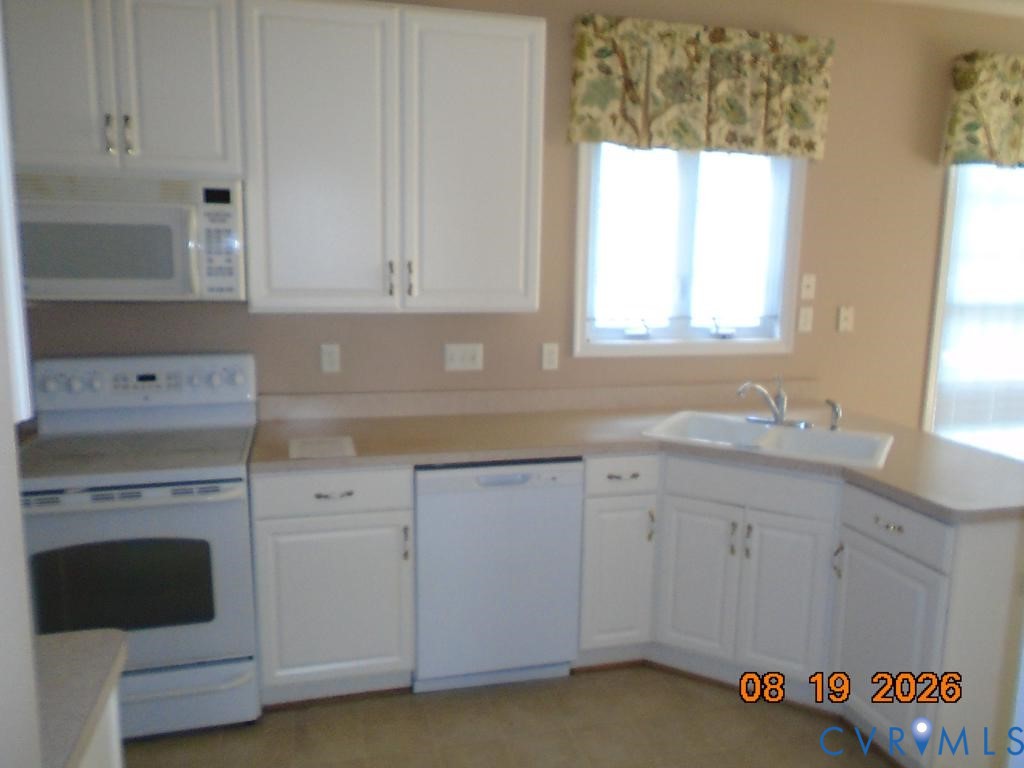White cabinetry, built-in microwave, white electric range, white dishwasher, and corner sink White cabinetry, built-in microwave, white electric range, white dishwasher, and corner sink